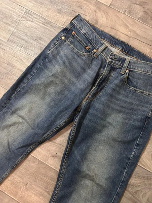 Levi's 514 blå jeans straight fit - Säljer ett par Levi's 514 jeans i klassisk blå tvätt med snygga slitningar. Modellen har rak passform, fem fickor och guldfärgade nitar. Jeansen har normal midja och är tillverkade i robust denim med Levi's ikoniska läderpatch bak.