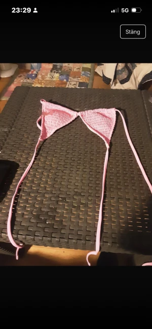 Rosa bikiniöverdel med smock och knyt - Supersöt rosa bikiniöverdel med smockad struktur och tunna knytband. Triangelmodell som ger en trendig och ungdomlig look, perfekt för stranden eller poolen. Ljusrosa färg och mjukt material som känns bekvämt mot huden.