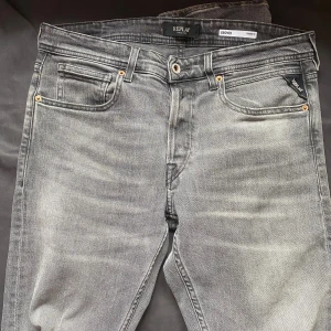 Replay Grover grå jeans straight fit - Säljer ett par Replay Grover jeans i snygg grå färg med straight fit. Klassisk femficksmodell med ljusa slitningar. Jeansen har metallknapp och dragkedja framtill, samt tydlig Replay-logga. Perfekta för en avslappnad och stilren look. W32/L32               Nypris 1600kr