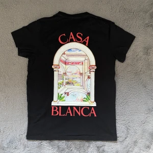 Svart Casa Blanca T-Shirt  - En svart t-shirt med röd text från Casa Blanca med ett unikt logg både på fram sidan och bak, som verkligen ger t-shirten en ”wow” effekt. PRISET KAN DISKUTERAS 