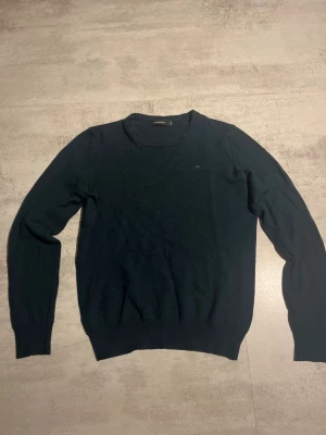 Mörkgrön stickad tröja J.Lindeberg - Snygg mörkgrön stickad tröja från J.Lindeberg i storlek S. Tröjan har rund hals, JL-logga på bröstet och ribbade muddar vid ärmslut och nederkant. Perfekt för dig som gillar stilrena och klassiska plagg med en modern touch. 1299kr nypris* 