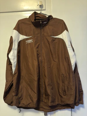 Brun vindjacka från Umbro - Köpt begagnad. Allmänt bra skick. Sitter som en oversize L eller en vanlig XL