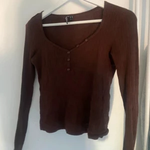 Brun ribbad långärmad topp Pieces - Brun långärmad topp från Pieces i ribbad bomullskvalitet. Toppen har v-ringning med dekorativa knappar framtill och sitter snyggt med en normal passform. Perfekt att styla med jeans eller kjol för en chill look.