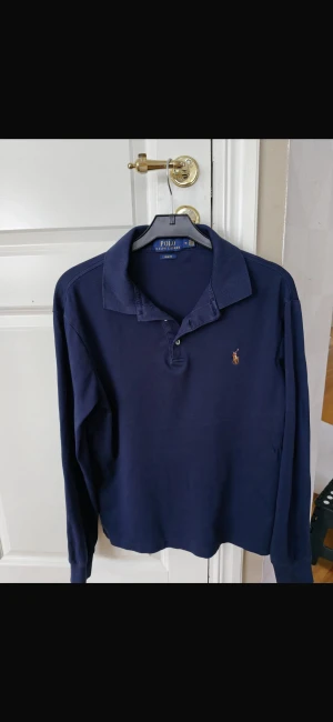 Polo Ralph Lauren tröja - Snygg marinblå långärmad pikétröja från Polo Ralph Lauren i slim fit. Klassisk krage, knappar vid halsen och ikoniska broderade loggan på bröstet. Perfekt för dig som gillar stilrena och tidlösa plagg. Materialet är mjuk bomull.