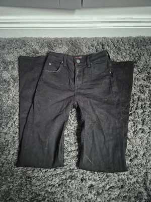 Svarta wide jeans från Lee - Säljer ett par svarta jeans från Lee med klassisk femficksdesign och breda ben. Jeansen har normal passform och är tillverkade i slitstarkt denimtyg. Snygga detaljer med Lee-logga på bakfickan och läderpatch i midjan.