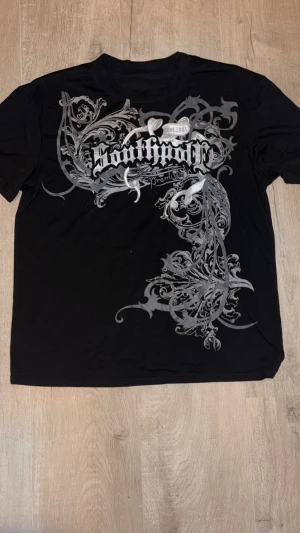 Svart Southpole t-shirt med tryck - Cool svart t-shirt från Southpole med stort grått och vitt grafiskt tryck på framsidan. Klassisk rund hals och korta ärmar. Materialet är mjuk bomull som känns skönt mot huden. Perfekt för dig som gillar streetwear och vill sticka ut med snygg design.