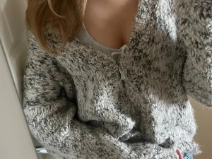 Gråmelerad stickad kofta från KappAhl - Mysig och chunky stickad kofta från KappAhl i gråmelerad ton. Koftan har långärmade ärmar, v-ringad hals och knytning framtill. Perfekt för lager-på-lager och chill dagar. Materialet är grovstickat och känns riktigt mjukt och fluffigt.