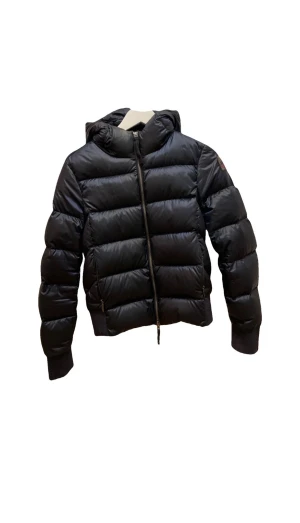 Svart pufferjacka Parajumpers Sheen S - Svart pufferjacka från Parajumpers, modell Sheen, i storlek S. Jackan har en snygg quiltad design med huva, dragkedja framtill och ribbade muddar. Materialet är glansigt och känns riktigt lyxigt, perfekt för kalla dagar. Köpt för ett år sedan, i väldigt bra skick. Enda tecken på användning är lite nopprig på insidan av mudden längst ner. Nypris 6 449kr