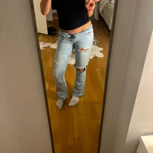 Ljusa slitna jeans - Säljer ett par ljusa jeans med slitningar på knäna och låren. De har en bootcut-stil och är lågmidjade, har hål på insida midja så man kan snöra in, och därmed göra midjan mindre