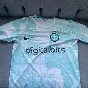 Inter Milan T-shirt  - Snygg fotbollströja från Nike i vit och mintgrön med världskarta som mönster. Tröjan har korta ärmar och Inter-logga på bröstet. Perfekt för fotbollsfans som vill sticka ut på planen eller läktaren.
