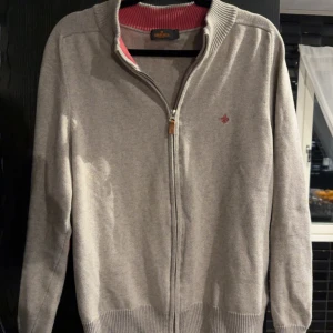  kofta från Morris - Grå/beige kofta från Morris med hel dragkedja och ribbad krage i rosa. Liten broderad logga på bröstet och rosa detaljer vid armbågarna. Stickad i mjukt material, perfekt för lager-på-lager. Snygg och stilren design som funkar till jeans eller chinos. Storlek S men sitter som M. Passar dig som är mellan 170-180cm. Priset kan diskuteras vid snabb affär 