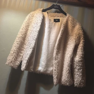”Ljus rosa”teddy kofta från H&M - Mysig och fluffig teddykofta från H&M i ljus rosa nästan intill vit färg. Korta  har långärmad design och är tillverkad i ett mjukt, syntetiskt material med lockig struktur. Perfekt för dig som vill ha en trendig och bekväm look under kyligare dagar.💕