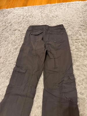 Lågmidjade Cargobyxor - Lågmidjade gråbruna cargobyxor från Brandy Melville. Justerbar midja och många fickor. Knappt använda så i mycket gott skick. Onesize men skulle säga att de passar XS/S. Mått: Innerbenslängd: 71 cm Midja: 38cm Grenmått: 25 cm Hör av er vid frågor/prisförslag!