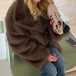 Brun pälsjacka med bred krage - Säljer en brun pälsjacka med bred krage och generös passform. I nyskick, Köpt på Jackie från märket neo noir. Jackan har långa ärmar och är tillverkad i mjukt, fluffigt material som ger en lyxig känsla. Perfekt för dig som vill sticka ut och hålla dig varm under kyliga dagar.