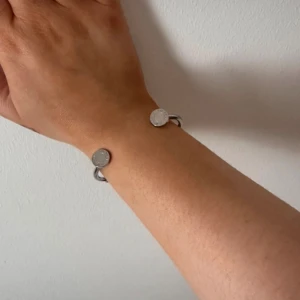 Silvrigt armband med rundade detaljer - Stilrent och minimalistiskt armband i silverfärgad metall med två runda plattor i ändarna. Öppen design som gör det enkelt att ta på och av. Perfekt för dig som gillar enkel och modern stil.