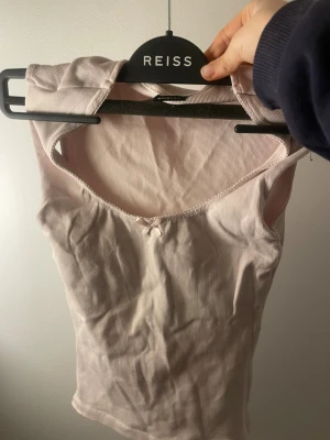 Ljusrosa ribbad linnetopp Gina Tricot - Supersöt ljusrosa linnetopp från Gina Tricot i ribbad bomull. Toppen är ärmlös med rundad halsringning och en liten rosett framtill som detalj. Perfekt att styla med jeans eller kjol för en chill och feminin look.