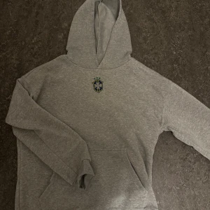 Grå hoodie med Brasilien-emblem - Säljer denna riktigt fina Brasilien hoodien, väldigt skönt material med ull på insidan. Säljer den för att jag tappat bort byxorna och inte längre vill ha tröjan själv. Skulle säga att den passar lite baggy för folk som har M och lite mer i längden för personer med storlek M. Riktigt fin tröja och skön även nu inför vintern, helt ny oanvänd. Priset kan diskuteras !🫡