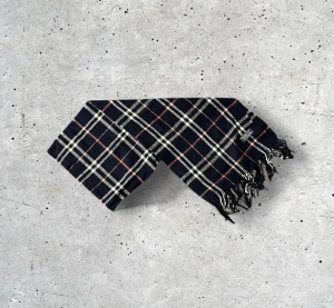 Burberry Scarf Mörkblå - ✨ Klassisk Burberry-halsduk i 100% ull – elegant mörkblå ✨ Säljer en tidlös Burberry-halsduk i en snygg och elegant mörkblå färg med det ikoniska rutmönstret. Tillverkad i 100% mjuk och värmande ull som känns lyxig, håller formen väl och ger en exklusiv känsla. En perfekt accessoar som lyfter både vardags- och festoutfits och passar året runt.  🧵 Skick: Mycket fint skick, varsamt använd 🌟 Känsla: Mjuk, varm och följsam 📦 Frakt: Skickas tryggt inom 24h 📏 Mått: Längd-150cm, Bredd-30cm