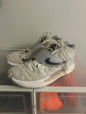 Nike KD 14 sneakers i grått och vitt - Nike KD 14 sneakers med coolt mönstrad mesh i ljusgrått och vitt, svart swoosh på sidan och transparent rem över snörningen. Skorna har rund tå, platt sula och detaljer i silver på hälen. Perfekt för dig som gillar basket eller vill ha en unik sneaker.