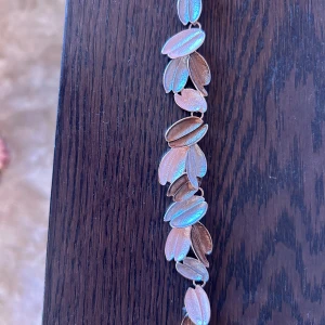 Roséguldfärgat armband med bladmotiv - Unikt armband i roséguldfärg med länkar formade som små blad. Bladen har en skimrande yta som reflekterar ljus i blå och rosa toner. Kedjan är tunn och elegant, perfekt för dig som gillar naturinspirerade detaljer och stilren design.