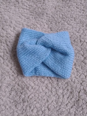 Ljusblå stickat pannband - Snyggt ljusblått stickat pannband med twistad front som jag gjort själv. Perfekt för att hålla öronen varma och ge en chill vibe till din look. Mjukt material och bred passform som sitter skönt på huvudet. Passar dig som gillar enkel och stilren accessoar.