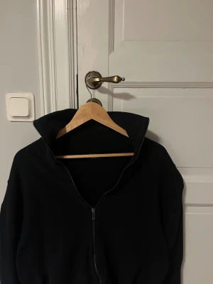 Svart ziptröja från Massimo Dutti - Svart långärmad ziptröja från Massimo Dutti med hög krage och stilren design. Tröjan har dragkedja framtill och är tillverkad i mjuk bomull, perfekt för chill dagar eller när du vill ha en clean look.