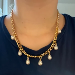 Guldhalsband med pärlhängen - Snyggt halsband i guldtonad kedja med droppformade vita pärlor som hänger längs hela halsbandet. Perfekt för dig som gillar statement-smycken och vill ha något som sticker ut lite extra. Kedjan är grov och pärlorna ger en lyxig känsla. Halsband 