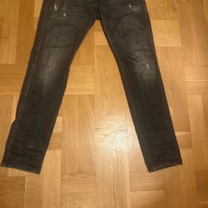 Replay mörka jeans, storlek 34/32 - Säljer ett par snygga Replay jeans i mörkgrå tvätt med raka ben och klassiska bakfickor. Jeansen är tillverkade av ekologisk bomull och har diskreta slitningar framtill för en cool look. Passar dig som gillar stilrena och bekväma jeans.