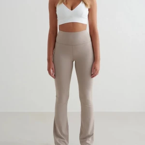 Beige flare leggings från Aim'n - Supersnygga beige leggings från Aim'n med hög midja och utsvängda ben. De är tillverkade i ett mjukt och stretchigt syntetmaterial som sitter tajt över höfterna och låren. Perfekta för dig som gillar en clean och sportig look.