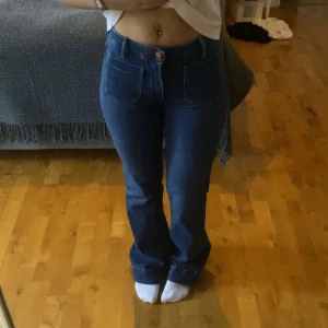 Blå bootcut jeans från Wrangler - Säljer ett par blå jeans från Wrangler med bootcut passform och hög midja. Jeansen har stora framfickor, klassiska bakfickor med Wrangler-logga och är tillverkade i jeansmaterial. Perfekta för dig som gillar retrovibbar och snygg siluett. W25/L32
