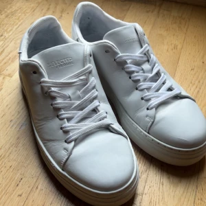 Vita sneakers från Selected Homme - Säljer ett par stilrena vita sneakers från Selected Homme i skinn. Klassisk modell med rund tå, platt sula och vita snören. Perfekta för dig som gillar minimalistisk och clean look. Tillverkade i Portugal och passar till det mesta.