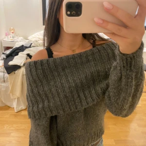 Mörkgrå offshoulder stickad tröja Gina Tricot - Supermysig mörkgrå stickad tröja från Gina Tricot med bred ribbad kant och offshoulder-modell. Perfekt till jeans och chunky smycken. Tröjan har lång ärm och är riktigt skön och varm för kyliga dagar.