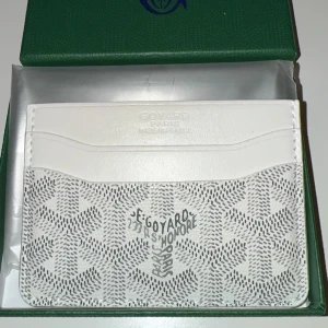 Vit plånbok med mönster - Snygg och stilren vit plånbok med deras ikoniska grafiska mönster i grått. Plånboken har flera fack för kort och är tillverkad i exklusivt skinn. Perfekt för dig som gillar lyxiga accessoarer med unik design.