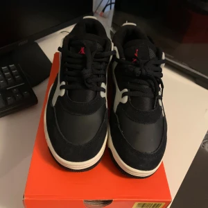 Nike Jordan sneakers svart/vit - Säljer ett par feta Nike Jordan 4 RM sneakers i svart och vitt med röda detaljer. Skorna har en chunky sula, snörning och coola paneler i mocka och syntet. Perfekta för dig som vill sticka ut med en klassisk streetwear-look.