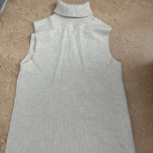 Ljusgrå ärmlös polotopp - Säljer en stilren ljusgrå polotopp med ribbad hög krage. Toppen är ärmlös och har en mjuk, stickad känsla som gör den perfekt för lager-på-lager. Enkel och clean design som funkar till många olika looks.