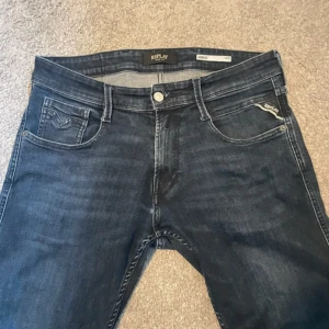 Replay Anbass  - Snygga Replay Anbass jeans i mörkblå tvätt med klassisk femficksdesign och diskreta slitningar. Jeansen har raka ben och normal passform W28 L29