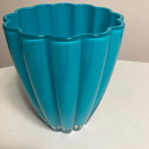 Vas  - Den här produkten är en blå, räfflad vas eller skål i plast eller glas, cirka 13 cm i diameter. Den har en modern, vågig design och är i mycket gott skick utan synliga repor eller skador. Perfekt som dekoration eller för blommor. Färgen är livfull och ytan är blank.