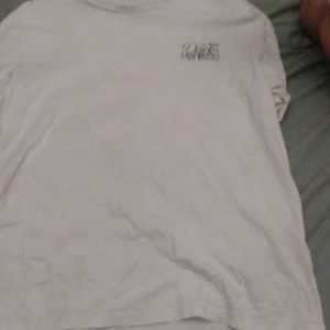 Vit t-shirt Jack & Jones Dark Manifesto - Vit t-shirt från Jack & Jones Originals med trycket 'Dark Manifesto' och coolt motiv på framsidan. Klassisk passform och rund hals. Tillverkad i mjuk bomull, perfekt för en avslappnad stil.