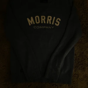Blå stickad tröja från Morris - Snygg blå stickad tröja från Morris med vit text 'MORRIS COMPANY' på bröstet. Tröjan har rund halsringning, ribbade muddar och är långärmad. Perfekt för dig som gillar klassisk och stilren look.