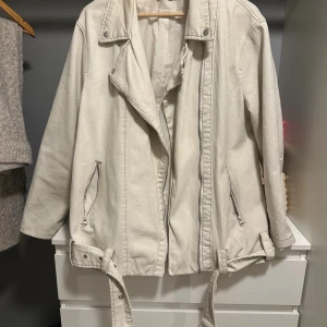 Vit bikerjacka från ASOS DESIGN - Säljer en vit bikerjacka från ASOS DESIGN i bomull. Jackan har klassisk krage, dragkedjor vid fickorna och framtill, samt bälte nedtill. Långärmad och med snygga detaljer som tryckknappar på kragen. Perfekt för dig som gillar stilrena och coola jackor.