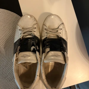 Valentino Garavani vita sneakers strl 42 - Säljer ett par vita Valentino Garavani sneakers med bred svart detalj över mitten. Klassisk rund tå, snörning och platt sula. Skorna är i skinn och har en stilren, modern look som passar till det mesta. Märkeslogga på plösen och insidan. Skriv vid fundering och lägg bud så får vi se om jag går med på det.