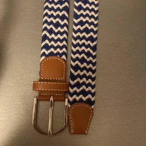 Randigt blåvitt flätat bälte - Säljer ett snyggt flätat bälte i blått och vitt med bruna skinn-detaljer och silverspänne. Skärpet är 1m (pris kan diskuteras)