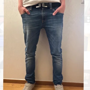 Ljusblå Nudie Jeans Storlek 28/32 - Säljer ett par ljusblå jeans från Nudie Jeans med klassiska orange sömmar och snygga detaljer på bakfickorna. Jeansen har normal midja och är tillverkade i mjukt denimtyg som sitter tajt hela vägen ner. Priset är inte hugget i sten!