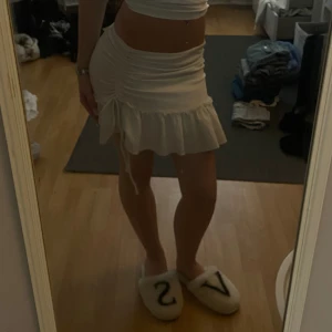 Vit volangkjol från Gina Tricot - Supersöt vit kortkjol från Gina Tricot i storlek XXS. Kjolen har volangkant nertill och snygg snörning på sidan som ger en extra detalj. Perfekt för dig som gillar en feminin och trendig stil. Materialet känns mjukt och stretchigt.