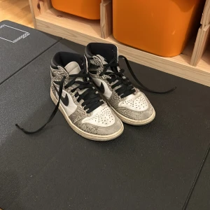 Nike Air Jordan 1 Elephant Print - Säljer ett par Nike Air Jordan 1 med ikoniskt elephant print i grått och svart. Skorna har svart swoosh, svarta snören och detaljer i vitt skinn. High-top modell med klassisk Jordan Wings-logga på sidan. Perfekta för dig som vill sticka ut med en unik sneaker. Original pris är ungefär 1500-2500kr.