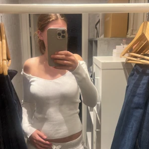 Vit ribbad offshoulder-top - Säljer en vit ribbad långärmad topp med offshoulder-modell och v-ringning. Toppen är figurnära och har en snygg croppad passform som framhäver axlarna. Perfekt för dig som gillar en stilren och trendig look.