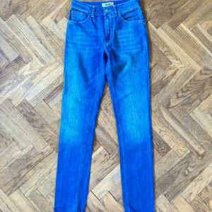 Blå skinny jeans från Acne, 27/32 - Snygga blå jeans från Acne i modellen Needle M-Mid Waist Lena. Klassisk femficksdesign, smal passform och medelblå tvätt. Tillverkade i bomull med lite elastan för extra stretch och komfort. Perfekta för dig som gillar stilrena och tajta jeans.