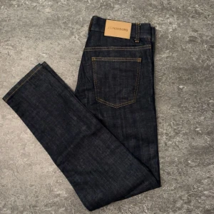 Mörkblå jeans från J.Lindeberg 29/32 - Snygga mörkblå jeans från J.Lindeberg i klassisk rak modell. Jeansen har kontrastsömmar, fem fickor och är tillverkade i slitstarkt denim. Perfekta för dig som gillar stilrena och tidlösa byxor med modern passform.