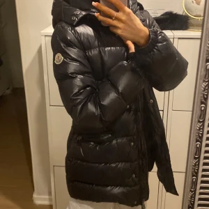 Svart dunjacka från Moncler - Säljer en snygg svart dunjacka från Moncler. Jackan har en glansig finish och är utrustad med en huva och dragkedja. Perfekt för kalla dagar när du vill hålla stilen. 🖤