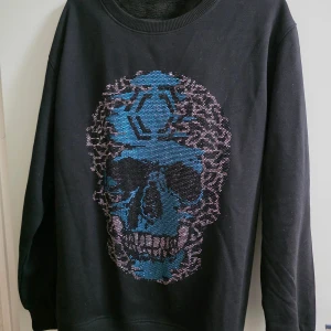 Svart sweatshirt PP - Cool svart sweatshirt med stort blått döskalletryck framtill i glittriga stenar. Tröjan har rund halsringning och långa ärmar. Mjuk insida i fleece och ribbade muddar vid ärmslut och nederkant. Perfekt för dig som gillar edgy streetstyle. Priset kan diskutera!!!!